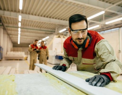 Carpintero con gafas de protección revisando un tablero en un taller de carpintería
