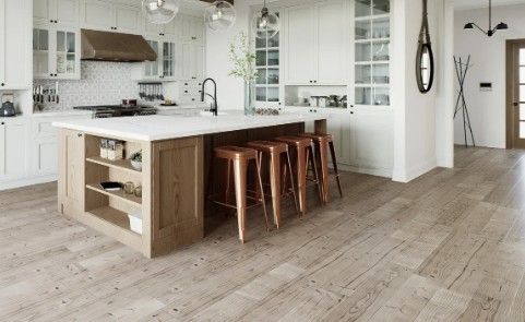 Cocina blanca con isla de madera, vitrinas altas y taburetes de cobre