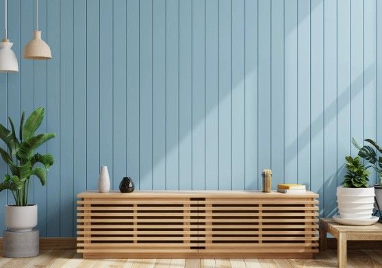 Mueble bajo de listones de madera maciza frente a una pared azul